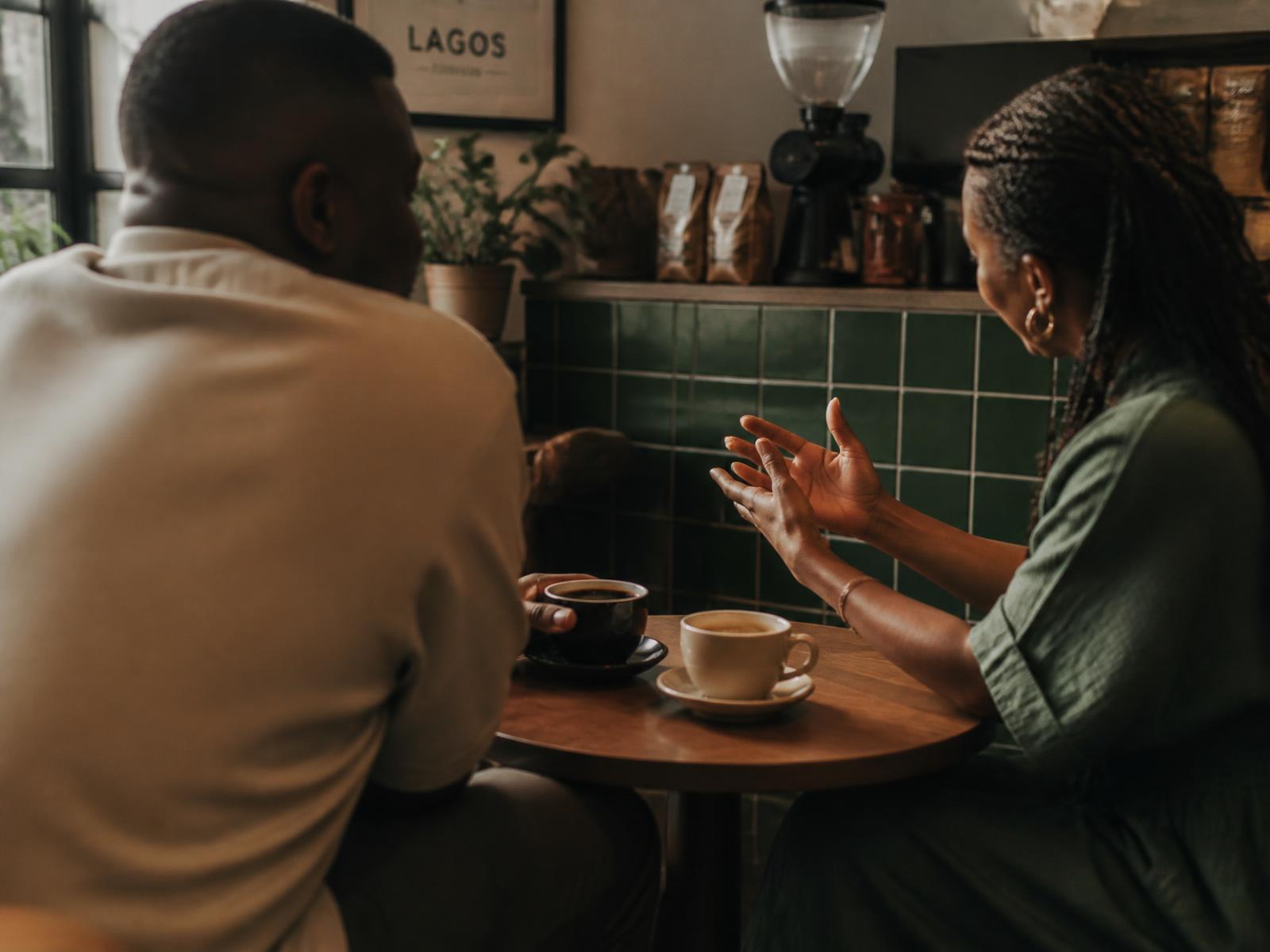 Two modern African adults in an honest conversation across a table in a Lagos coffee shop